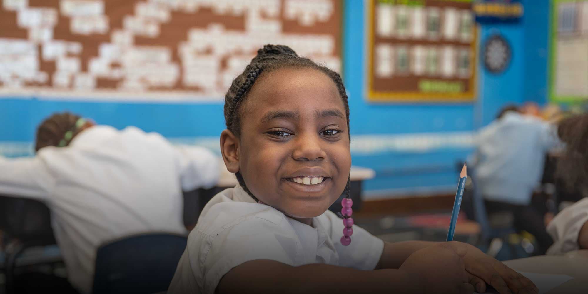Smiling student holding a pencil at a classroom desk.